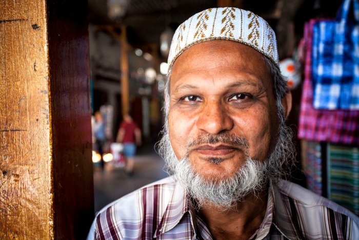 Close up street photography portrait of the man with white beard and hat in a market