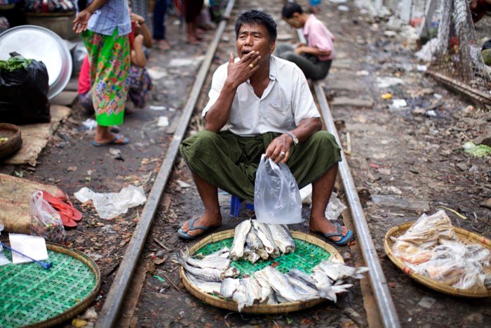 сцена рыбного рынка, мужчина сидит между железнодорожными путями с корзиной рыбы перед собой. уличная фотография
