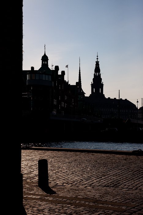 силуэты городских зданий на фоне светлого неба, на фоне тенистой улицы и реки в Копенгагене
