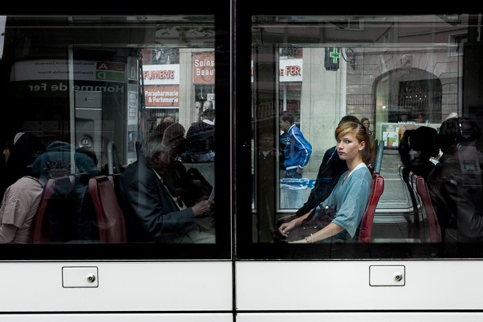 Вид из окна трамвая с молодой женщиной, смотрящей прямо в камеру. Городская фотография