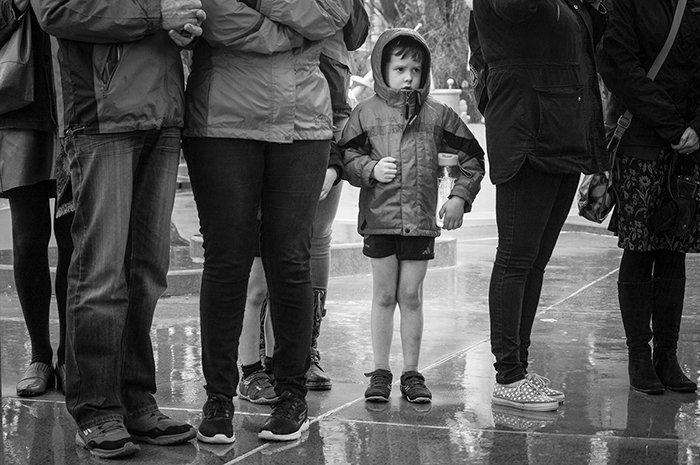 Черно-белая уличная фотография маленького мальчика в центре группы взрослых под дождем. Советы по уличной фотографии