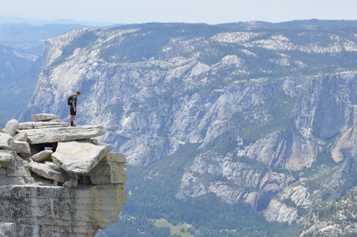 Человек, стоящий на краю обрыва с впечатляющим горным пейзажем позади него, демонстрирует баланс размера и веса в фотографии