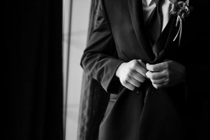 Черно-белая свадебная фотография жениха, застегивающего пиджак крупным планом