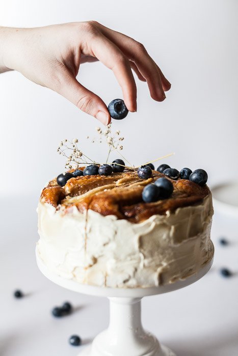 Восхитительный снимок руки, кладущей чернику на торт на белом фоне, сделанный макрообъективом для съемки натюрморта