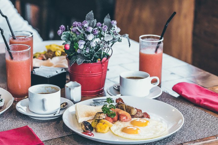 Красивая фуд-фотография обеденного стола с тарелкой еды, чашками кофе и стаканами сока, снятая макрообъективом для съемки натюрмортов