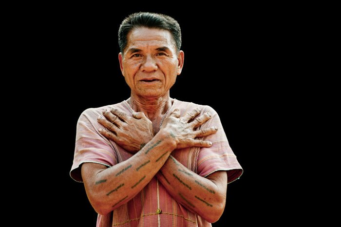 Каренский мужчина демонстрирует свои традиционные татуировки на фоне черной земли в студии портретной фотографии на открытом воздухе.