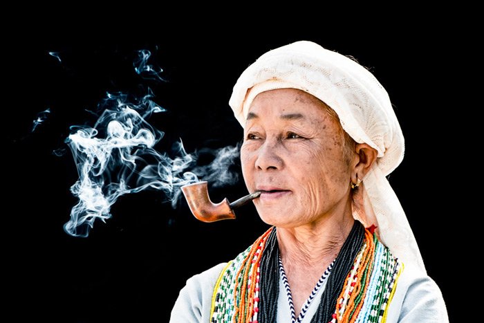 Фотография тайской женщины, курящей трубку на черном фоне в студии портретной фотографии на открытом воздухе.