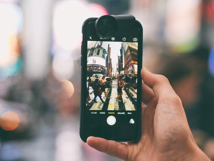 Рука, держащая смартфон, фотографирует оживленную уличную сцену