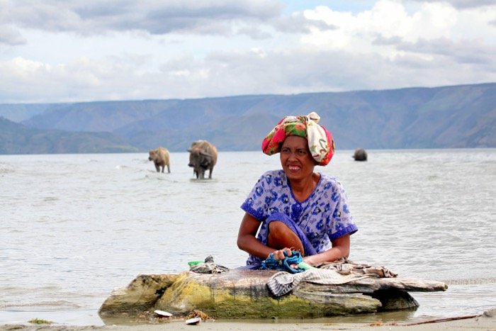 Travel photography of a woman washing clothes in the sea with cows in the background- travel photography checklist.