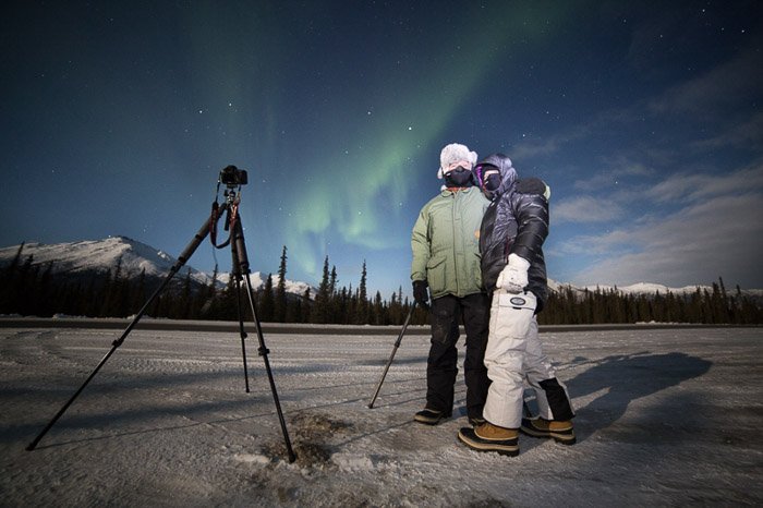 Фотография двух фотографов с камерой и штативом, снимающих северное сияние. Зимняя фотография.