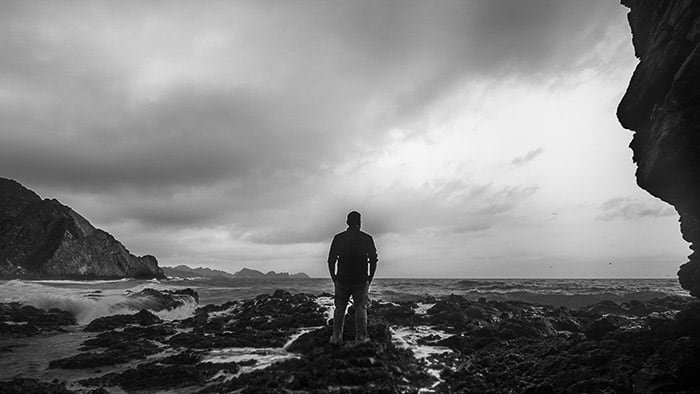 Монохромная прибрежная фотография человека, стоящего на скалах и смотрящего в сторону океана с соотношением сторон 16:9