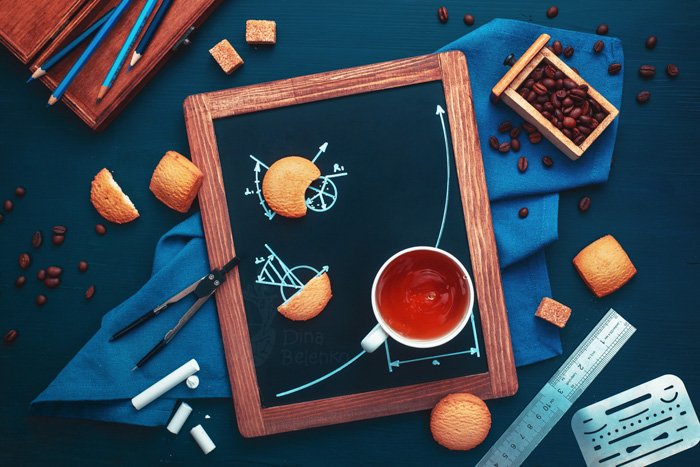 Натюрморт с использованием кофейных чашек, печенья, меловой доски, карандашей и кофейных зерен, чтобы рассказать историю о школьнике, делающем домашнее задание по геометрии