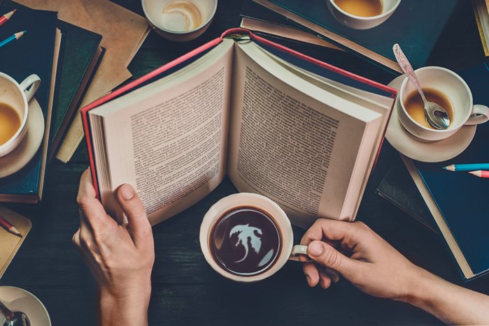Концептуальный натюрморт, изображающий человека, читающего фэнтезийную книгу и видящего дракона в отражении кофейной чашки.