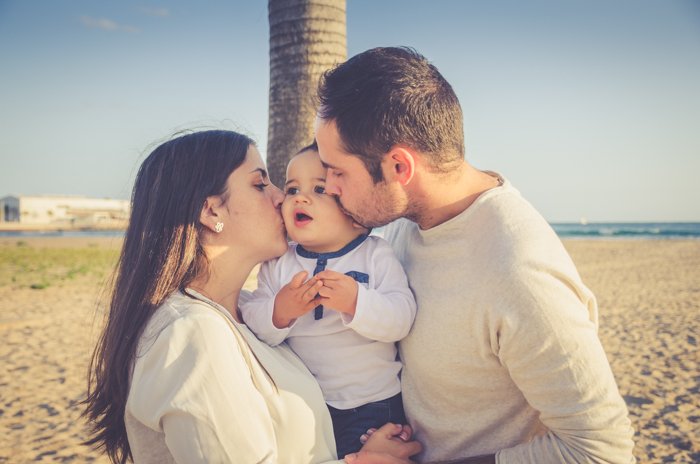 Милый портрет мужчины и женщины, держащих маленького ребенка и целующих его в щечки на пляже - композиция семейных портретов