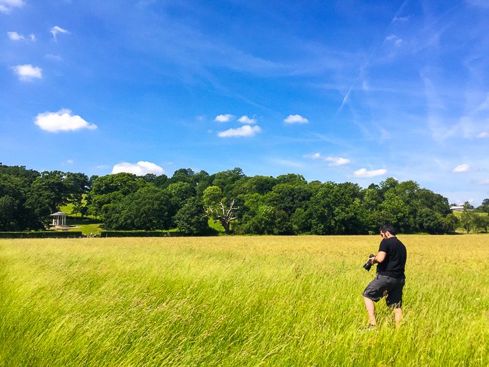 Фотограф проверяет настройки своей камеры в травянистом пейзаже в ясный день с голубым небом