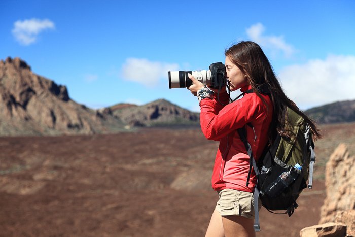 Женщина-фотограф регулирует настройки камеры в скалистом ландшафте с голубым небом