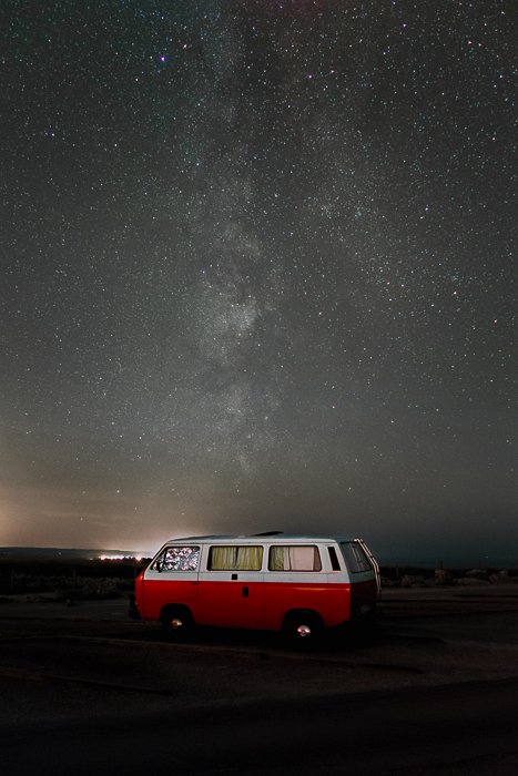 Изображение красного фургона, припаркованного под впечатляющим звездным небом, после использования фокусного суммирования для удаления звездных следов