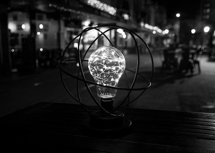 Черно-белый уличный снимок ночной скульптуры из лампочек на деревянном столе