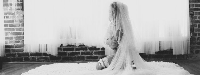 Эфирная черно-белая будуарная фотография девушки в свадебном платье, сидящей на ковре