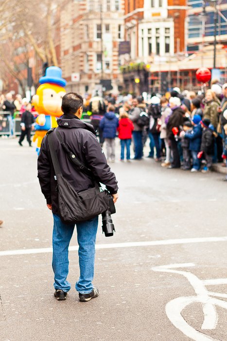 Мужчина с фотоаппаратурой стоит на улице и наблюдает за фестивальной толпой на заднем плане