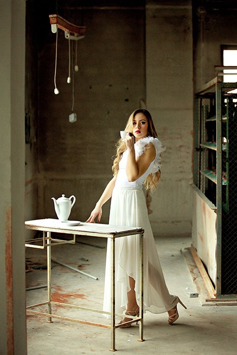 Художественный портрет светловолосой женщины, позирующей в минимальной кухонной зоне в белом вечернем платье