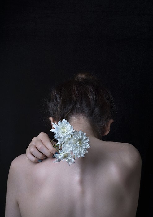 Художественная портретная фотография спины женщины-модели, держащей белые цветы в направлении камеры