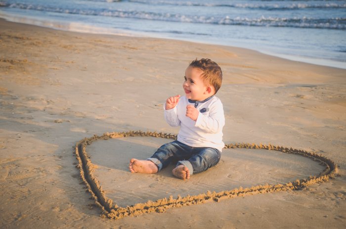 Молодой парень сидит в центре любовного сердца, нарисованного на песке, креативные идеи для пляжной фотографии.