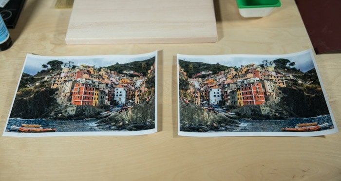 Две одинаковые фотографии ярко раскрашенного прибрежного города, лежащие на деревянной доске, готовящейся к переносу фото на дерево