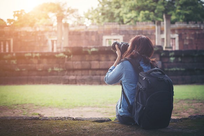 Женщина-фотограф сидит на траве и делает снимок