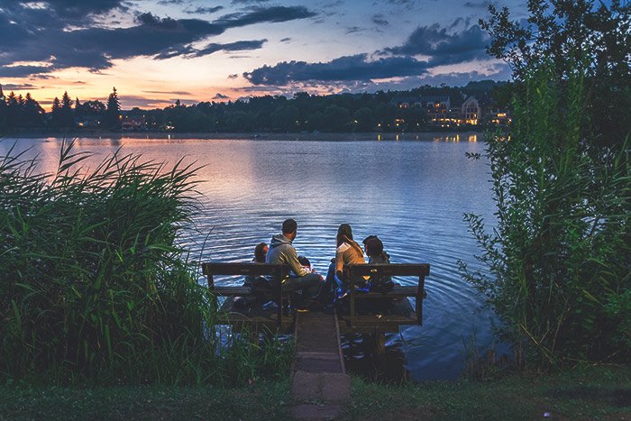 Фотография семьи, сидящей у озера на закате