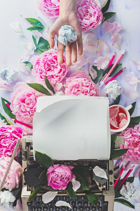 Яркий и воздушный плоский натюрморт с пишущей машинкой, розовыми розами и рукой, держащей скомканный бумажный шарик
