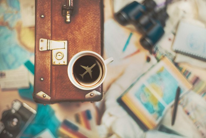 Натюрморт на тему путешествий с чашкой кофе, сидящей на чемодане с изображением самолета внутри