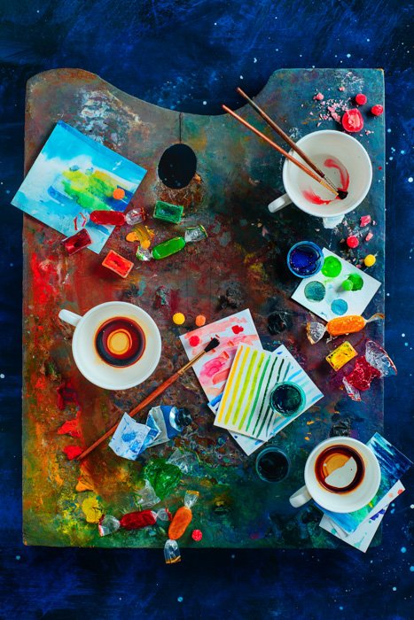 Яркий художественный тематический натюрморт с палитрой художника, покрытой краской, чашками, кистями и другими художественными материалами