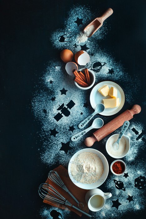 Мрачный и атмосферный пищевой плоский натюрморт с мукой, яйцами, маслом и кухонной утварью на темной поверхности