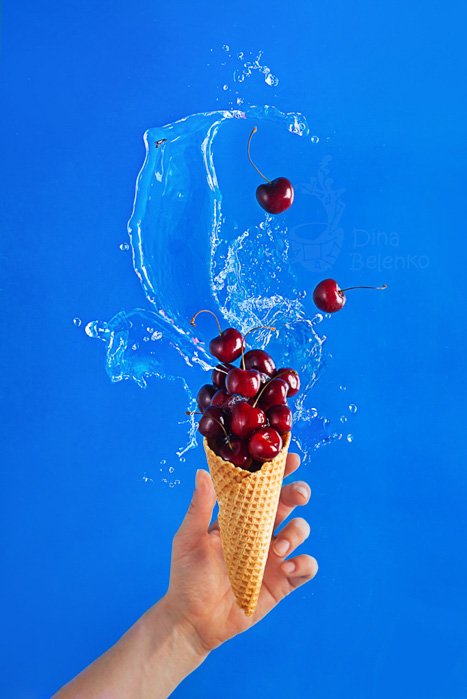 Рука, держащая рожок мороженого с вишней на светло-голубом фоне для плоской фотографии