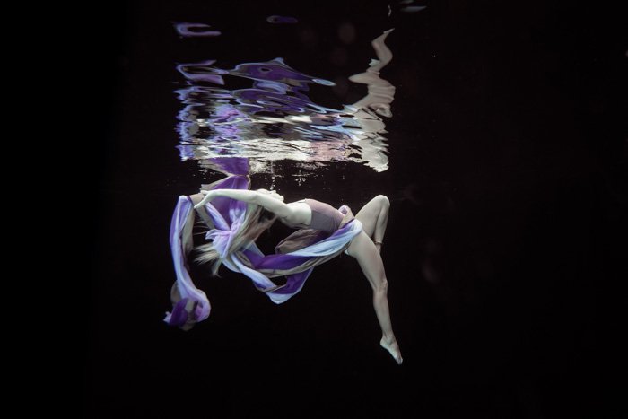 Потрясающая подводная фотография девушки, позирующей с фиолетовой тканью во время плавания под водой