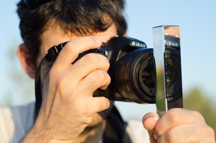 Фотограф держит фотопризму перед объективом своей цифровой зеркальной фотокамеры Canon