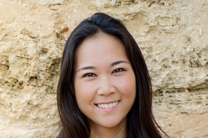 headshot of smiling asian woman in front of sandy stone wall