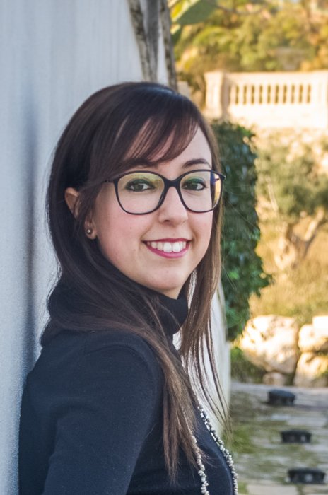 cropped portrait of brunette with eyeglasses leaning against a while wall on a sunny afternoon