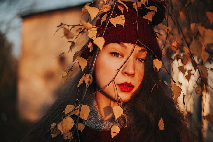 Красивый портрет девушки на природе с ветками деревьев перед лицом, снятый с использованием рассеянного освещения для создания мечтательного эффекта