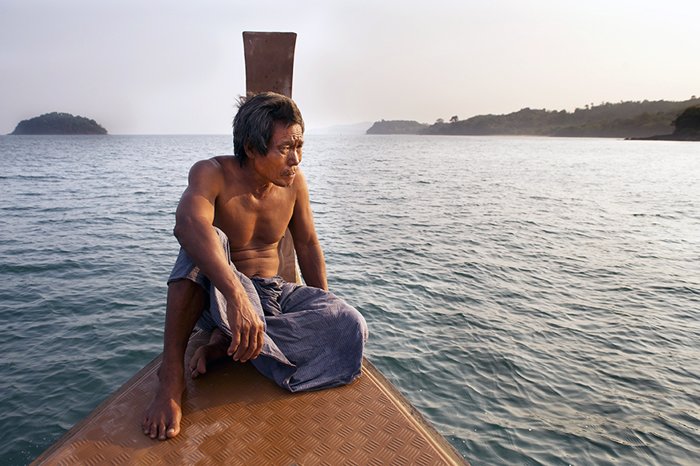 Человек, сидящий на маленькой деревянной лодке в море