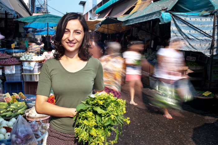 Молодая женщина стоит на оживленном рынке. Снято с длинной выдержкой, чтобы размыть движение людей.