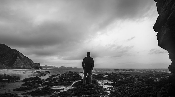 Черно-белый снимок человека на пляже, смотрящего в сторону океана
