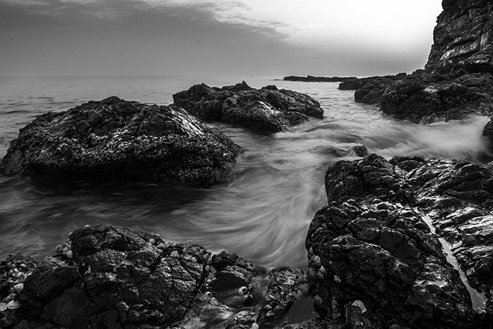 Черно-белый снимок скалистого пляжа с мягким туманным эффектом воды вокруг скал и утесов