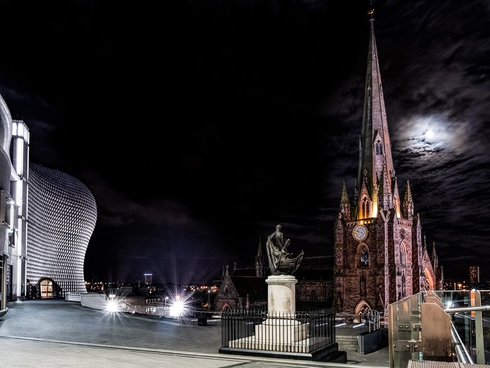 Святой Мартин в Буллринге, со статуей Нельсона и торговым центром Буллринг в Бирмингеме. Строение освещено на фоне темного неба, луна жутко светит из-за облаков