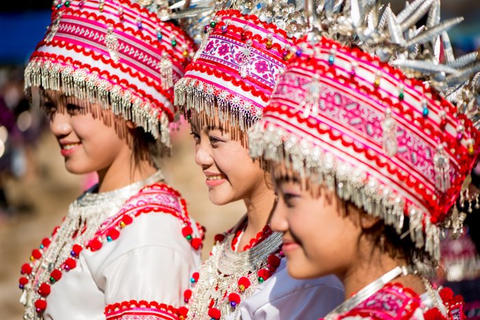 три улыбающиеся девушки в красно-белых традиционных головных уборах и костюмах