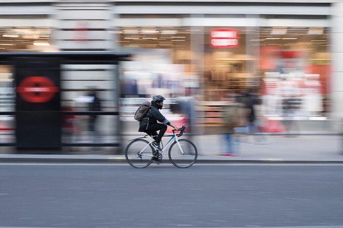 Человек едет на велосипеде по городу, фон творчески размыт из-за использования длинной выдержки