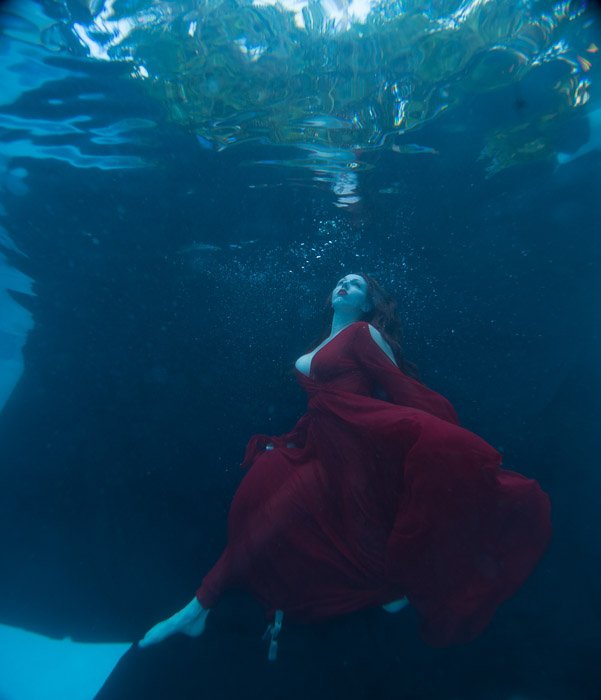 Красивая женщина в струящемся красном платье позирует под водой