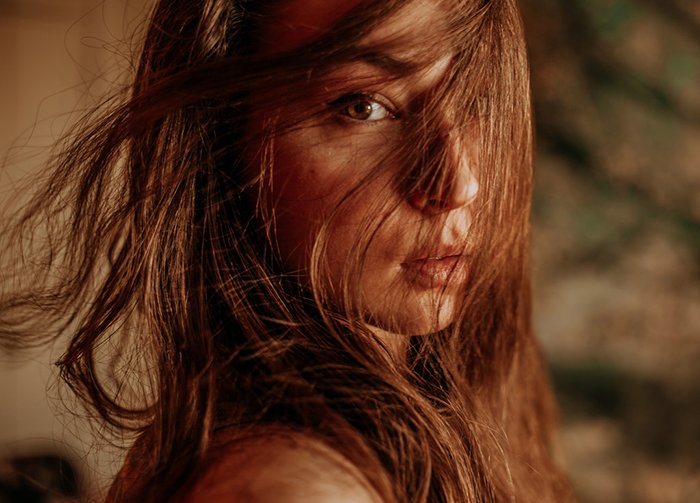 Красивый портрет девушки с волосами, закрывающими лицо, снятый с использованием рассеянного освещения для создания мечтательного эффекта