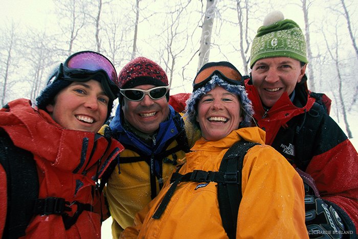четыре туриста улыбаются в камеру во время приключенческой фотосессии, снег и голые деревья позади них